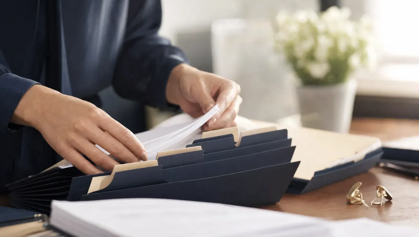 Hands collating pages into tidy labeled folders — missing returns being assembled